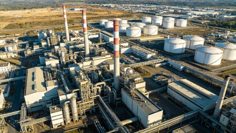 Aerial overhead view of large industrial chemical plant with processing units, pipelines, tall red-and-white chimneys and white storage tanks