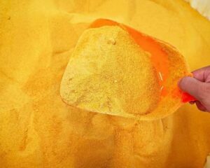 Yellow PAC powder on an orange sampling scoop above a bag of powder